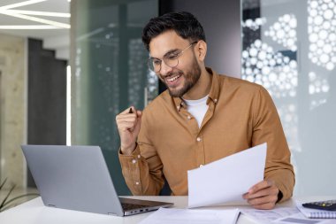 Memlekette çalışırken, bilgisayarını kullanıp belgeleri incelerken başarısını kutlarken mutlu bir profesyonel. Uzak çalışma ve iş başarıları konsepti.