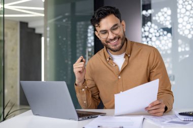 Modern ofis ortamında belgelere bakıp gülümseyen bir iş adamı. Profesyonel, üretken ve işte mutlu..