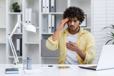 Stresli bir adam ofiste çalışırken akıllı telefonunu tutar. Bir iş meselesi yüzünden hayal kırıklığına uğramış ve endişeli görünüyor..