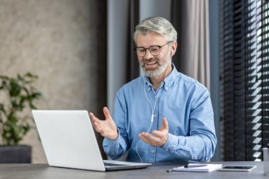 Üst sınıftan bir adam, bir sohbete dalmış, evindeki bir video görüşmesine neşeyle katılıyor.