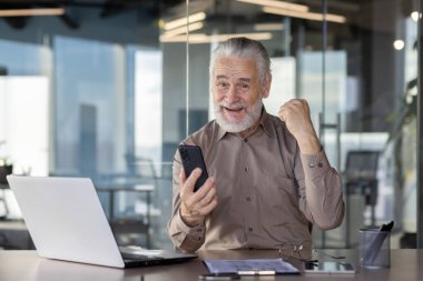 Görevdeki yaşlı işadamı çağrı üzerine sevinçle kutlama yapıyor, kariyerinde zafer ve mutluluk gösteriyor.
