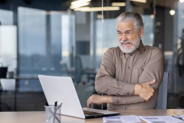 Uzun zamandır ofiste laptopla çalışan yaşlı, kır saçlı bir adam. İş yerindeki olgun bir işadamı, elinde şiddetli bir ağrı hisseder..