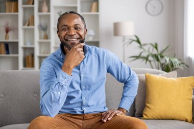 Huzurlu bir ev ortamında, mutlu bir yüzü olan bir adam bitkilerle ve kitaplarla dolu bir odada rahatlar, bir anlık huzur ve rahatlık için rahat ve huzurlu bir ortam yaratır.