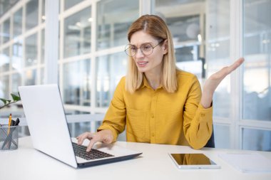 Modern ofis ortamında dizüstü bilgisayar kullanan kafası karışmış profesyonel bir kadın belirsizlik ve tefekkür gösteriyor..