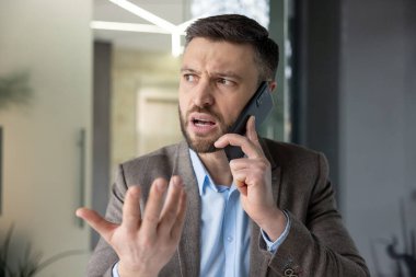 Takım elbiseli, hayal kırıklığına uğramış bir işadamı hararetli bir telefon görüşmesi yapar ve ofis ortamında el hareketleriyle duygularını ifade eder..