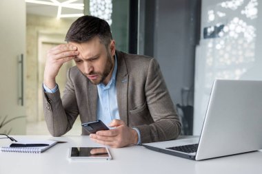 Modern bir ofisteki stresli bir işadamı endişeli ve hayal kırıklığına uğramış bir şekilde telefonundan kötü haberler alıyor..