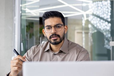 Kendine güvenen genç iş adamları, bir dizüstü bilgisayarla meşgulken modern ofis ortamında, odaklanmış ve konuşuyorlar.