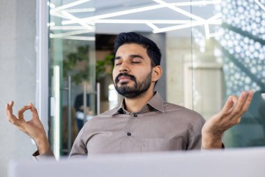 Modern bir ofis alanında farkındalık meditasyonu uygulayan bir iş adamı, zihinsel refahı ve stres rahatlığını teşvik ediyor