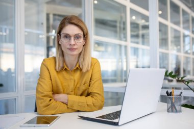 Bilgisayarı, tableti ve kalemleri olan modern bir ofiste masa başında oturan kendine güvenen bir iş kadını. Profesyonel ve odaklanmış atmosfer.