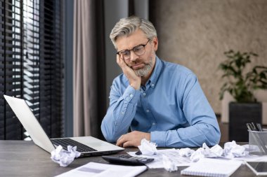 Üst düzey bir adam laptopta çalışırken stresli hissediyor buruşmuş kağıtlarla dolu, işindeki hayal kırıklığını gösteriyor..