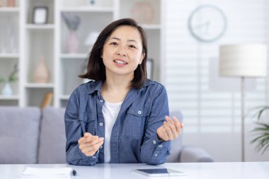 Asyalı bir kadın video görüşmesi yapıyor, modern bir oturma odası ortamından sohbet ediyor ve iletişim kuruyor..