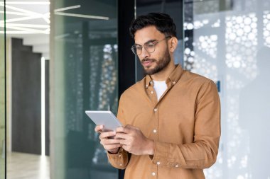 Modern ofis ortamında dijital tabletine odaklanan, odaklanan ve modern teknolojiyi kullanan genç bir profesyonel adam..