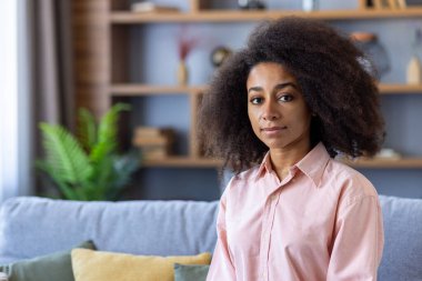 Evdeki bir kanepede oturan genç bir kadının portresi, arka planda bir kitaplıkla rahatlamış görünüyor..