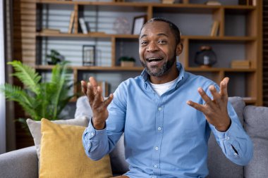 Modern bir oturma odasında rahat bir koltukta otururken görüntülü konuşma yapan neşeli bir adam..