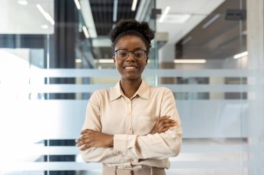 Modern bir ofis alanında kolları çapraz duran kendinden emin genç profesyonel bir kadın. Profesyonel çevre, kariyer başarısı.