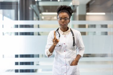 Steteskoplu ciddi bir kadın doktor modern ofis ortamında uyarı jesti yapıyor..