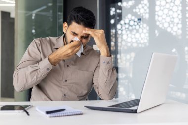 Hasta ve genç bir Hintli adam büroda oturuyor ve burnunun aktığı bir peçeteyle burnunu siliyor. Kendini iyi hissetmiyor..