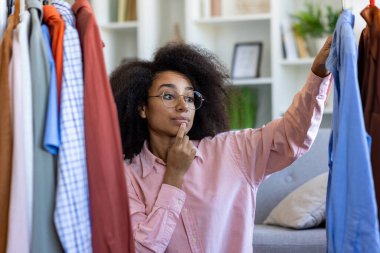 Elbiselerini özenle seçen bir kadın, bir ev ortamında moda seçimleri üzerine kafa yoruyor..