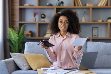 Bilgisayarında çalışırken mali durumunu hesap makinesi ve evrak işleriyle idare eden kendine güvenen genç bir kadın..