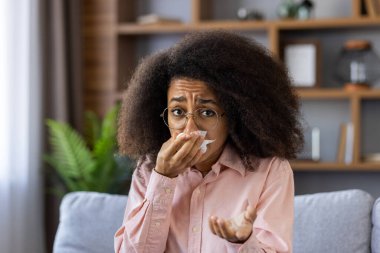 Sıkıntılı bir kadın çevrimiçi terapi seansına katılıyor, ağlıyor ve elinde mendil tutarken doğrudan kameraya bakıyor..