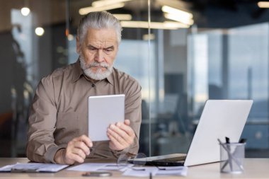 Bir ofis ortamında dijital tablet kullanan yaşlı bir işadamı. Modern bir çalışma alanında teknoloji, iş ve kıdemli profesyoneller kavramı.