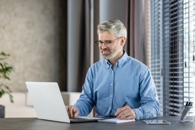 Modern, profesyonel bir ortamda ofis masasında dizüstü bilgisayarda çalışan gülümseyen bir iş adamı. Profesyonel, modern ofis ortamı ve üretkenlik kavramı.