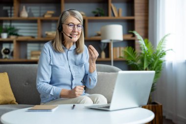 Mutlu son sınıf öğrencisi bir kadının evinde videosu var, gülümsüyor ve laptopuyla iletişim kuruyor. Rahat ve modern ev ortamları.