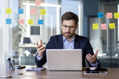 Modern ofis ortamındaki sanal toplantı sırasında cam duvarda yapışkan notlarla konuşan bir iş adamı. Profesyonel tartışma, uzaktan çalışma ve dijital iletişim kavramı.