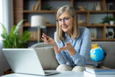 Üst düzey kadın öğretmen evinden online bir ders veriyor, dizüstü bilgisayara bakarken jestlerle anlatıyor. Kurulum, sanal bir öğretim ortamını gösteren eğitim materyallerini içeriyor.