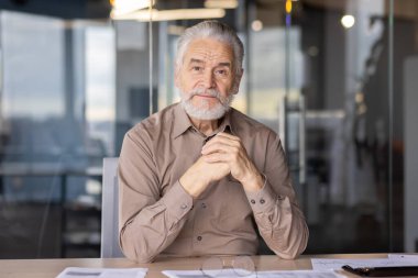 Modern bir ofis ortamında katlanmış ellerle güvenle oturan kıdemli işadamı. Olgun profesyoneller deneyim ve bilgelik yayar. İş, yürütme ve liderlik için ideal