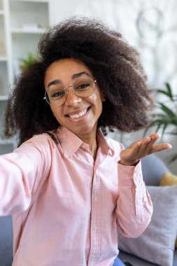 Positive and cheerful woman with glasses smiling and waving during a video call on her phone at home. Friendly and inviting, she embodies happiness and connectivity through modern technology. clipart