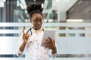 Steteskop takan kadın doktor modern ofiste video araması için tablet kullanıyor. Doktor sanal danışmanlık yapıyor, hastayla iletişim kuruyor. Teknoloji kullanan profesyonel sağlık çalışanı