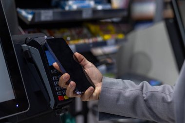 Yakın plan görüntü, akıllı telefondan yapılan ödemeleri gösteriyor. Perakende mağazasında işlem için dijital cüzdan kullanan biri. Nakit ödemeler, kolaylık ve modern teknoloji kavramı.