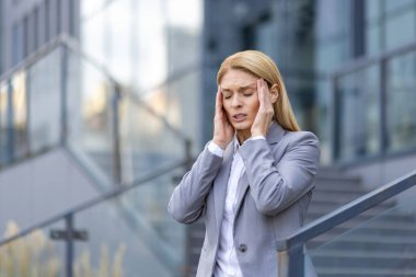 İş kadını ofis binasının önünde dikilirken stres ve baş ağrısı çekiyor. İş kıyafeti giymiş profesyonel bir kadın kendini çok kötü hissediyor. İş stresi ve akıl sağlığı kavramı