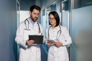 Hastane koridorunda hasta kayıtlarını tartışan tıp uzmanları. Beyaz önlüklü, steteskoplu kadın ve erkek sohbet ediyorlar. Tıbbi danışmanlık ve takım çalışması.