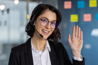 Modern ofis ortamında kulaklık takmış gülümseyen bir iş kadını. Mesleki kıyafet ve arkadaş canlısı tavır müşteri desteği, iletişim ve pozitifliği öneriyor.