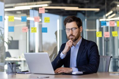 Ciddi düşünen iş adamının portresi, dizüstü bilgisayarlı bir adam kameraya bakıyor, iş yerinde deneyimli bir işçi, yatırımcı stratejisi düşünen bir yatırımcı..