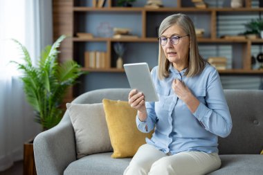 Yaşlı bir kadın, evde kanepede otururken hayal kırıklığı ve endişe göstererek psikoloğuyla sanal istişarede bulunuyor. Konsept zihinsel sağlık ve çevrimiçi terapiyi içerir