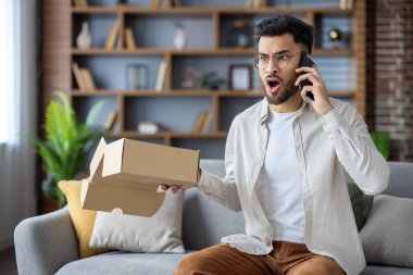 Adam elinde boş bir kutuyla kanepede oturuyor ve telefonda sinirli bir ifadeyle konuşuyor. Hayal kırıklığı ve müşteri hizmetleri sorunları kavramı