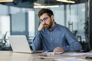 Modern ofiste dizüstü bilgisayarda çalışırken motivasyonsuz görünen bir iş adamı. Ofis çalışanı can sıkıntısı ve hayal kırıklığı hissediyor. İş yeri verimsizliği ve motivasyon kavramı eksikliği