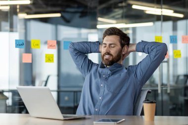 Kendinden ve bitirdiği işten memnun olan genç adam, büroda oturur ve dinlenir. Gözlerini kapadı ve ellerini başının arkasına attı, gülümseyerek..
