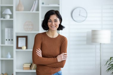 Kendine güveni tam bir kadın modern bir ofiste kitap rafları ve saatlerle gülümsüyor. İş, meslek ve yaşam tarzı kavramları için mükemmel..