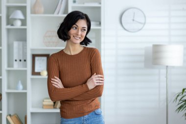 Modern bir ofiste gündelik giysiler içinde gülümseyen genç ve çekici bir kadın, kollarını göğsüne bağlıyor ve rüya gibi yan tarafa bakıyor..
