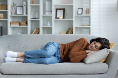 Genç bir kadın evinde dinleniyor, kanepede uzanıyor ve rahatça uyuyor, kafasının altında iki elini bir arada tutuyor..