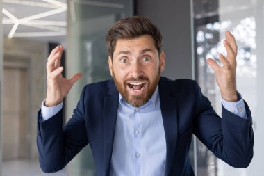 Takım elbiseli coşkulu bir işadamı ofis ortamında şaşkınlık ve neşe ifade eder. Başarılı ya da beklenmedik iyi haberleri simgeler..
