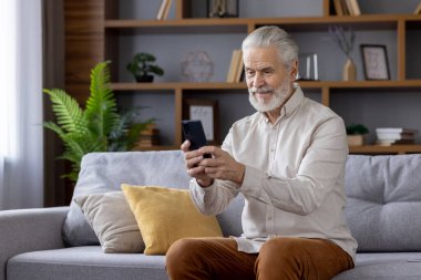 Oturma odasındaki kanepede oturan son sınıf öğrencisi akıllı telefon kullanıyor ve gülümsüyor. Teknoloji, iletişim ve eğlence kavramı.