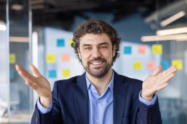 Çağdaş ofiste görüntülü konuşma sırasında gülümseyen ve el kol hareketi yapan kendinden emin bir işadamı. Günlük konuşma, bağlantı ve başarılı iletişim kavramı