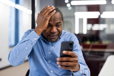 Ofisteki üzgün adam sıkıntılı görünürken elinde akıllı telefon tutuyor. Endişe, stres ya da hüsran gösteren bir iş adamı. Kötü haber, iş baskısı veya teknik sorunlar kavramı.