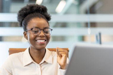 Modern ofiste bilgisayar üzerinde çalışırken gözlüklü mutlu iş kadını başarısını kutluyor. Kendine güvenen ve başarılı kadın profesyonel başarıyı ya da iş yerinde dönüm noktasını.