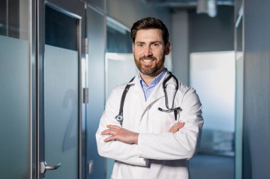 Hastane koridorunda kolları bağlı duran güler yüzlü doktor. Beyaz önlük ve steteskop giyen bir tıp uzmanı. Sağlık, tıbbi bakım ve profesyonel doktor konsepti..
